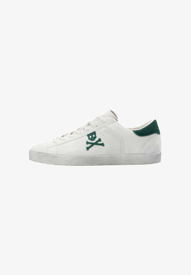 Zapatilla de ante blanca con un tabique de talón de ante verde, que presenta un logo de calavera y huesos cruzados verde en el costado y una suela de goma texturizada gris.