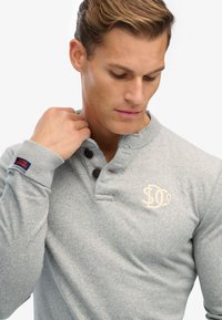 Grijze lange mouwen henley shirt gemaakt van zachte stof, met een klassieke kraag, drie knopen en een subtiele logo op de borst.