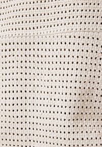 Vævet taske i lys beige med et tekstureret design, der har sammenfletninger og en let blank overflade.