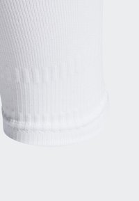 Bílé ribované ponožky s tkanou texturou, které mají zpevněnou patu a špičku a hladký manžetový okraj. Jednoduchý a nezdobený design.
