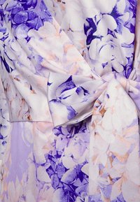 Textilie s květinovým vzorem v purpurových a světle růžových tónech, s měkkým, texturovaným povrchem. Obsahuje detail zavázaného pásu pro přiléhavý vzhled.