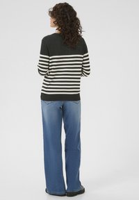 Pull rayé noir et blanc à col rond, porté avec un jean large bleu clair. Cheveux bouclés visibles. Style simple et décontracté.