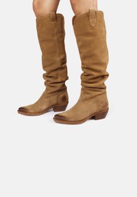 Bottes en daim marron mi-hautes avec un design décontracté, bout rond, petit talon empilé et logo discret sur le côté.