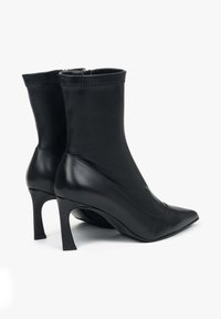 Černé kožené kotníkové boty na podpatku s špičatou špičkou, štíhlými stiletto podpatky a hladkým matným povrchem. Mají zipový uzávěr na zadní straně.