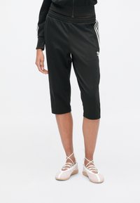 Μαύρο αθλητικό κάπρι παντελόνι με ομαλή υφή, ελαστική μέση και λευκές λωρίδες στα πλάγια. Συνδυασμένο με ροζ αθλητικά παπούτσια με κορδόνια.