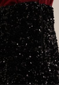 Svart paljettkjol med en figurnära design, som har en strukturerad yta och en dold dragkedja baktill.