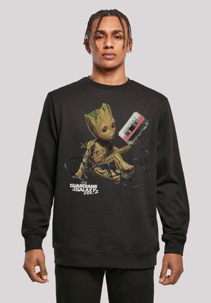 Svart hettegenser med et grafikk av Groot som holder et kassettbånd, med fargerike detaljer og tekst for "Guardians of the Galaxy Vol. 2."