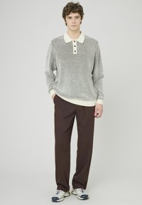 Pull en tricot gris à manches courtes avec un col crème et trois boutons, associé à un pantalon marron foncé et des baskets grises.