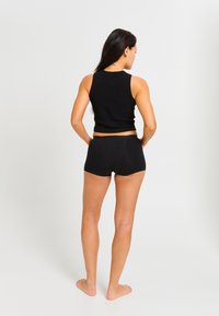 Haut sans manches noir associé à un short noir. Le tissu est lisse et ajusté ; le design est simple, sans motifs ni accents visibles.