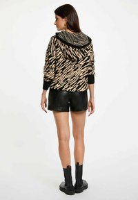 Beige en zwarte dierenprint hoodie met patroon, voorzien van een koord in de capuchon en ribgebreide manchetten, gedragen met zwarte leren shorts en enkelboots.