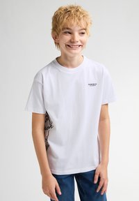 Bílý bavlněný tričko s malým černým logem na prsou a černou grafickou designovou aplikací na boku. Krátké rukávy, volný střih.