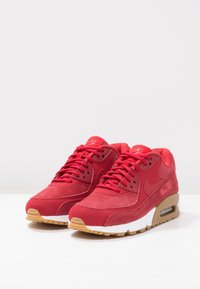 Röda Nike Air Max-sneakers med material av mocka och nät, med en vit mellansole och sula av gummigummi. Snörning och logotyper i matchande röd.