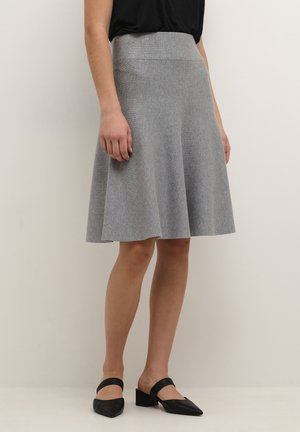 Jupe grise évasée en tissu texturé, avec une taille haute et un ourlet au-dessus du genou, associée à des chaussures noires à enfiler.