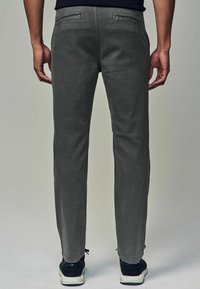 Grå chinos med slim fit, der har to baglommer, minimal tekstur, og som er parret med sorte sneakers med hvide såler.
