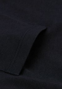 Ciemnoniebieska tkanina o gładkiej fakturze, z zagiętym brzegiem i widocznymi detalami przeszycia. Widok z bliska ukazuje drobne, równomierne sploty.