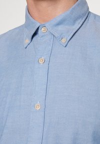 Ljusblått bomullsskjorta med knapp-down krage, som har fyra rundade knappar och subtila texturdetaljer.