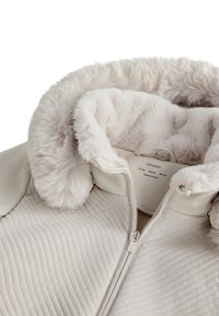 Beige gesteppte Jacke mit weichem Kunstfellkragen, ausgestattet mit einem Reißverschluss und einer glatten, strukturierten Oberfläche. Innenschild sichtbar.