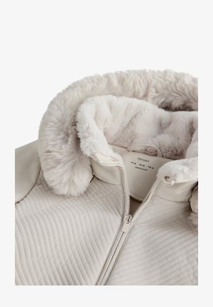 Beige quilted jacket with a soft faux fur collar, featuring a zip closure and a smooth textured finish. Inside label visible.