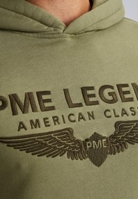 Olive green hoodie featuring brown embroidered text "PME LEGEND AMERICAN CLASSIC" and winged emblem graphics on the chest.
