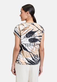 Short-sleeve blouse in soft fabric, featuring a nature-inspired print in beige, black, and white. Text reads "Beauty of Nature."