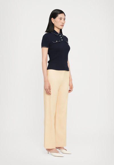Navy ribbed polo shirt with collar and pocket details, paired with pale yellow wide-leg trousers and white slip-on heels.