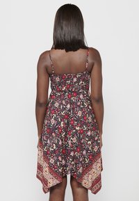 Robe florale multicolore avec des bretelles fines réglables, un buste smocké et un ourlet asymétrique doté d'une bordure à motifs rouges et dorés.