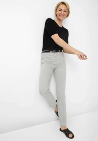 Pantalons slim gris clair avec poches avant, associés à un haut noir à manches courtes côtelé et des sandales noires à enfiler. Design simple.