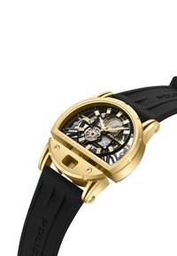 Czarny zegarek na gumowym pasku ze złotą stalową obudową. Posiada szkieletowy cyferblat z srebrnymi akcentami, wyraźne znaczniki godzin oraz charakterystyczny design.