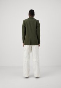 Blazer verde oliva su misura con spalle strutturate, abbinato a pantaloni cargo crema dotati di ampie tasche e orli risvoltati.