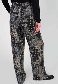 Pantalons noirs à motifs paisley avec une taille élastique, présentant des motifs dorés et argentés intricats sur un matériau fluide. Coupe droite.