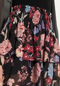 Vestido com padrão floral e cintura franzida em tons de preto, vermelho e azul. Apresenta camadas em babados e tecido leve.