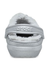 Silvriga Crocs-sandaler med mjuk vit pälsfoder, texturerat ovandel och en välvd baksnodd. Sulan är robust och något upphöjd.