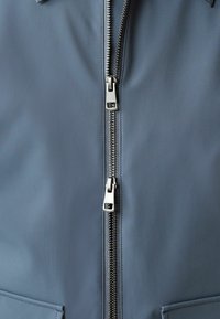 Pelēka rāvējslēdzēja džinsa jaka ar metālisku rāvējslēdzēju, gludu tekstūru un minimālistisku dizainu bez redzamām rakstām vai rotājumiem.