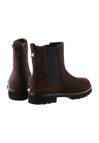 Brown suede ankle boots featuring elastic side panels, a rear zipper, and perforated detailing at the toe. Thick black rubber soles.