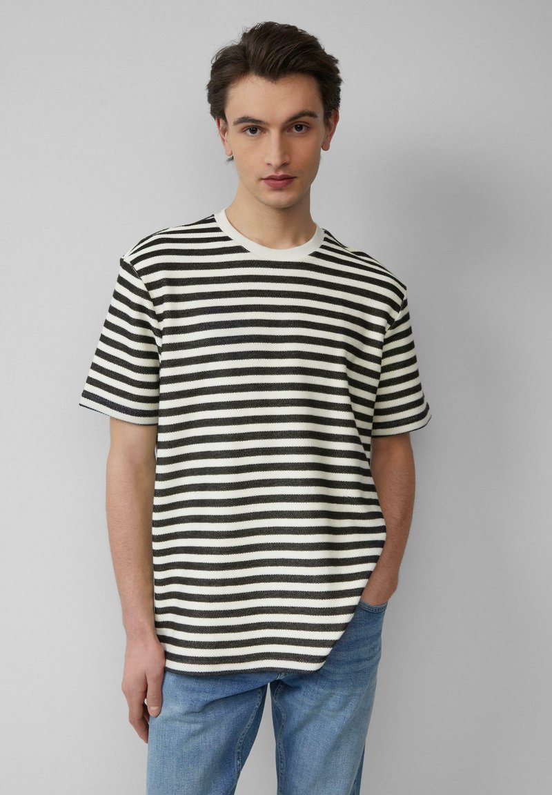 Zwart-wit gestreepte korteboomshirt met een ronde hals, textuurstof en een ontspannen pasvorm, gedragen met blauwe spijkerbroek.