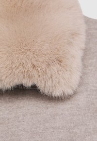 Mjuk beige pälskrage fäst vid en ljusbeige ullkappa, som visar detaljerad textur och tyg i närbild.