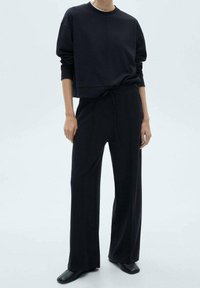 Sweat-shirt noir court à manches longues et col rond, associé à un pantalon noir ample avec une taille à cordon.