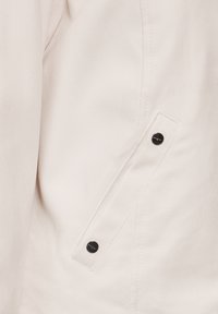 Giacca bianca in canvas con tasca a patta chiusa da bottoni neri, cuciture visibili e una texture liscia.