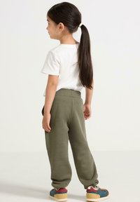 Hvid t-shirt i bomuld og olivengrønne sweatpants med en afslappet pasform og elastisk talje, parret med multikolore træningssko.