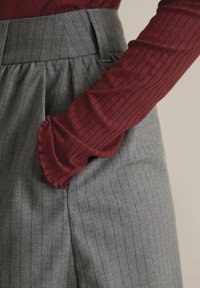 Szürke csíkos nadrág, redőzött dizájnnal, sima derékrésszel. Bordó, hosszú ujjú felső bordázott textúrával és fodros mandzsettával.