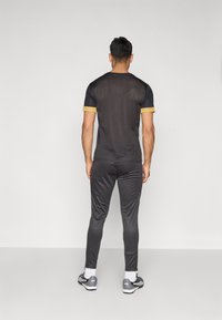 Μαύρο αθλητικό πουκάμισο με κοντά μανίκια και χρυσό περίγραμμα, σε συνδυασμό με ταιριαστό σκούρο παντελόνι. Διαθέτει κομψή, λεία υφή.