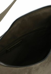 Innenseite der olivgrünen Wildledertasche mit einem Reißverschluss und glatter Fütterung. Verfügt über einen schwarzen Reißverschlusslauf und ein kleines Etikett an der Seite.