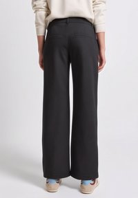 Pantalon noir à jambes larges en tissu lisse, comprenant une taille ajustée, deux poches arrière et une silhouette décontractée.