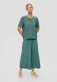 Turkusowy dwuczęściowy strój składający się z bluzki z krótkim rękawem i spodni z szerokimi nogawkami, wykonany z teksturowanej tkaniny, uzupełniony o plecione sandały.