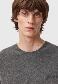 Dunkelgrauer Strickpullover mit Rundhalsausschnitt, der eine dezente Textur und ein besticktes Logodetail auf der Brust aufweist.