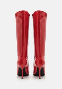 Red glossy knee-high boots with a pointed toe and high stiletto heel. Features a rear zipper closure and smooth, shiny texture.