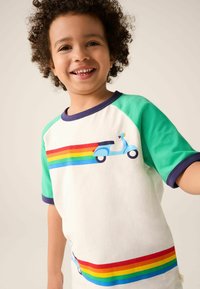 T-krekls ar baltu ķermeni, zaļām piedurknēm un tumši zilu apdari. Tam ir zila skūtera grafika un varavīksnes svītras pa krūtīm un apakšmalu.