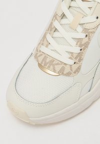 Adidași albi cu materiale din plasă și texturate, accente crem, șireturi plate și un detaliu cu logo metalic aurit pe lateral.