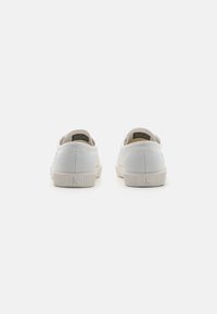 Witte canvas sneakers met getextureerde stof, ronde neus, rubberen zool en subtiele branding aan de achterkant. Minimalistisch ontwerp en neutrale kleur.