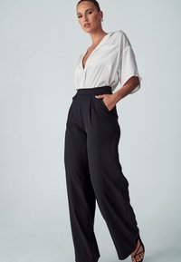 Witte blouse met korte mouwen, een kraag en zakken, gecombineerd met hoog-taille zwarte, losse broek en zwarte sandalen met bandjes.